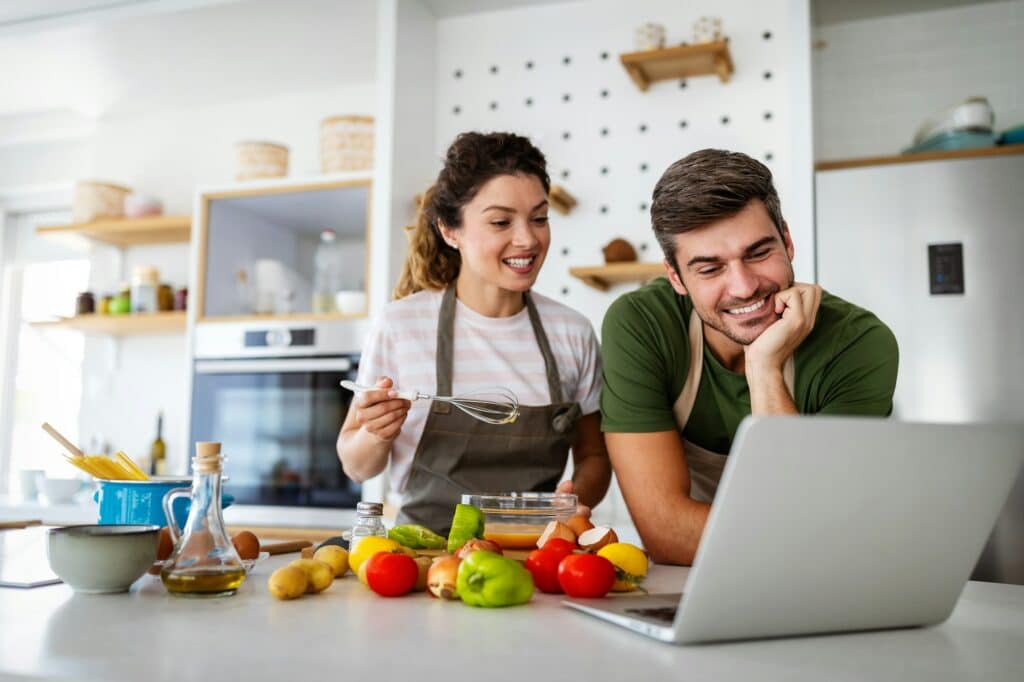 Happy young couple enjoying making a meal plan from NutriPOM's Holistic Nutrition Programs in their kitchen.